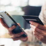 A person in a striped shirt holds a smartphone and a credit card, appearing to make an online purchase. The scene conveys modern technology and convenience.