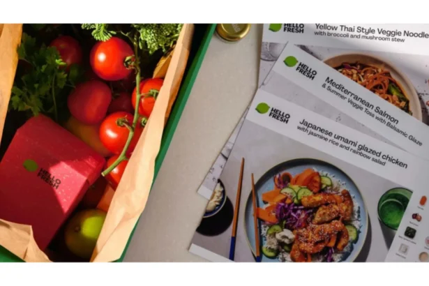 HelloFresh meal kit box filled with fresh produce, including tomatoes and herbs, alongside recipe cards featuring a selection of prepared meal options.