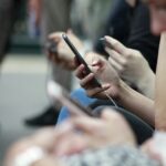 Close-up of people sitting side by side using smartphones, with multiple hands holding mobile devices, illustrating social media and digital connectivity.