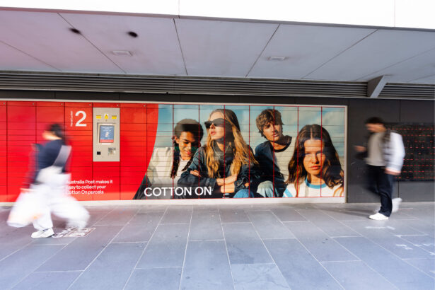 Australia Post parcel lockers featuring Cotton On advertising, with pedestrians walking past.