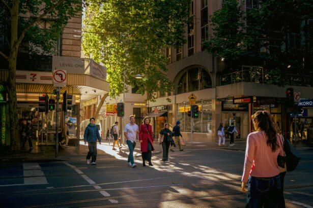 Pedestrians crossing a busy Melbourne CBD street in afternoon sunlight, surrounded by shops and city buildings.