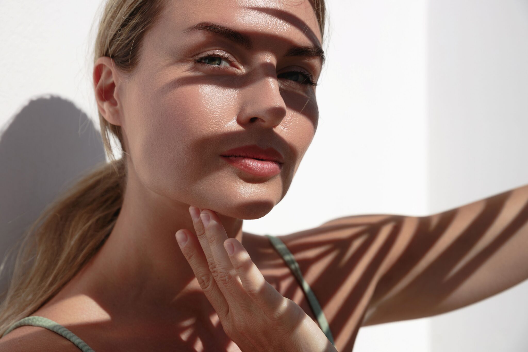 Close-up portrait of a woman in natural sunlight, with striped shadows cast across her face and shoulders.