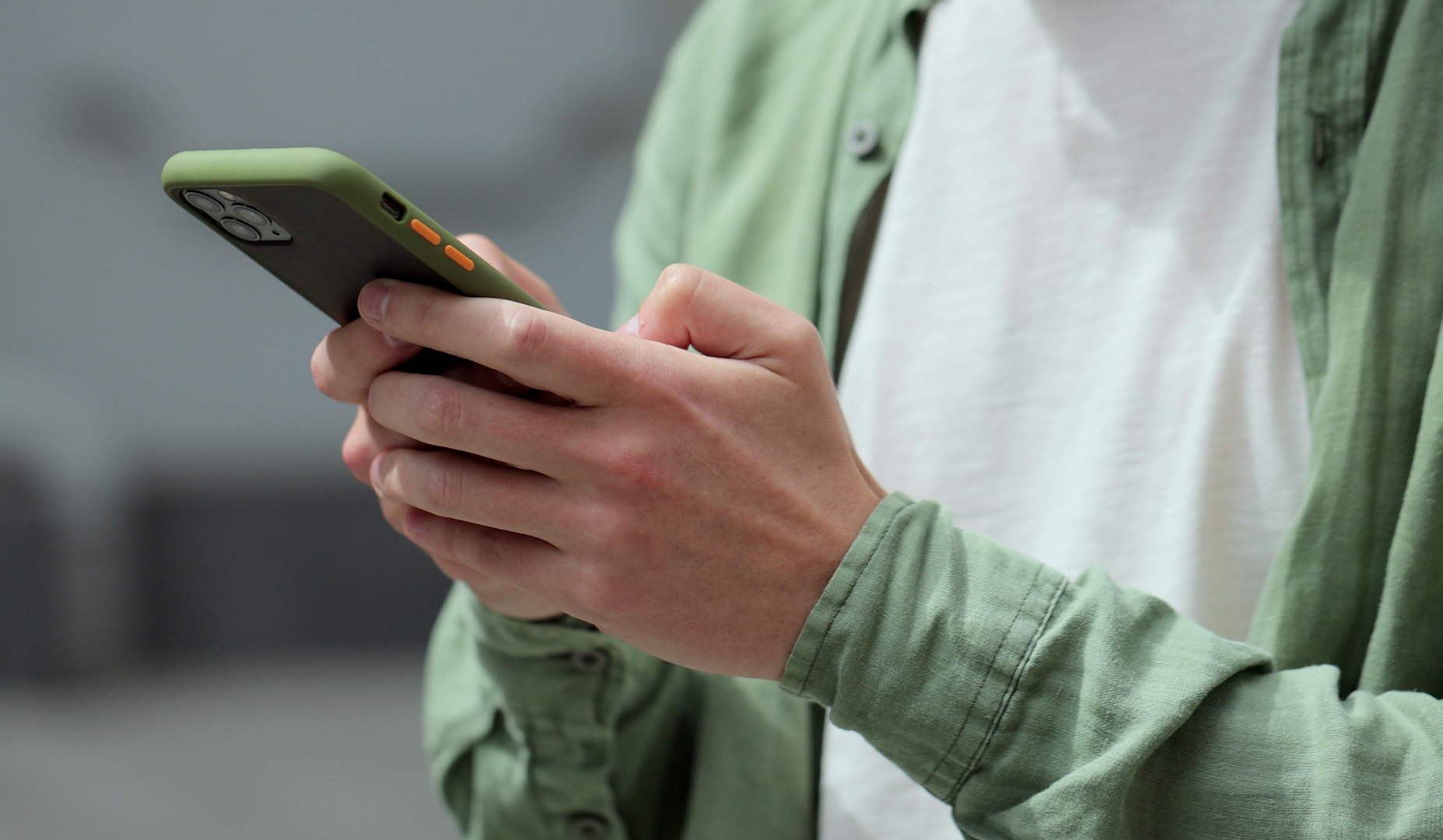 Close-up of a person wearing a green shirt using a smartphone held in both hands.