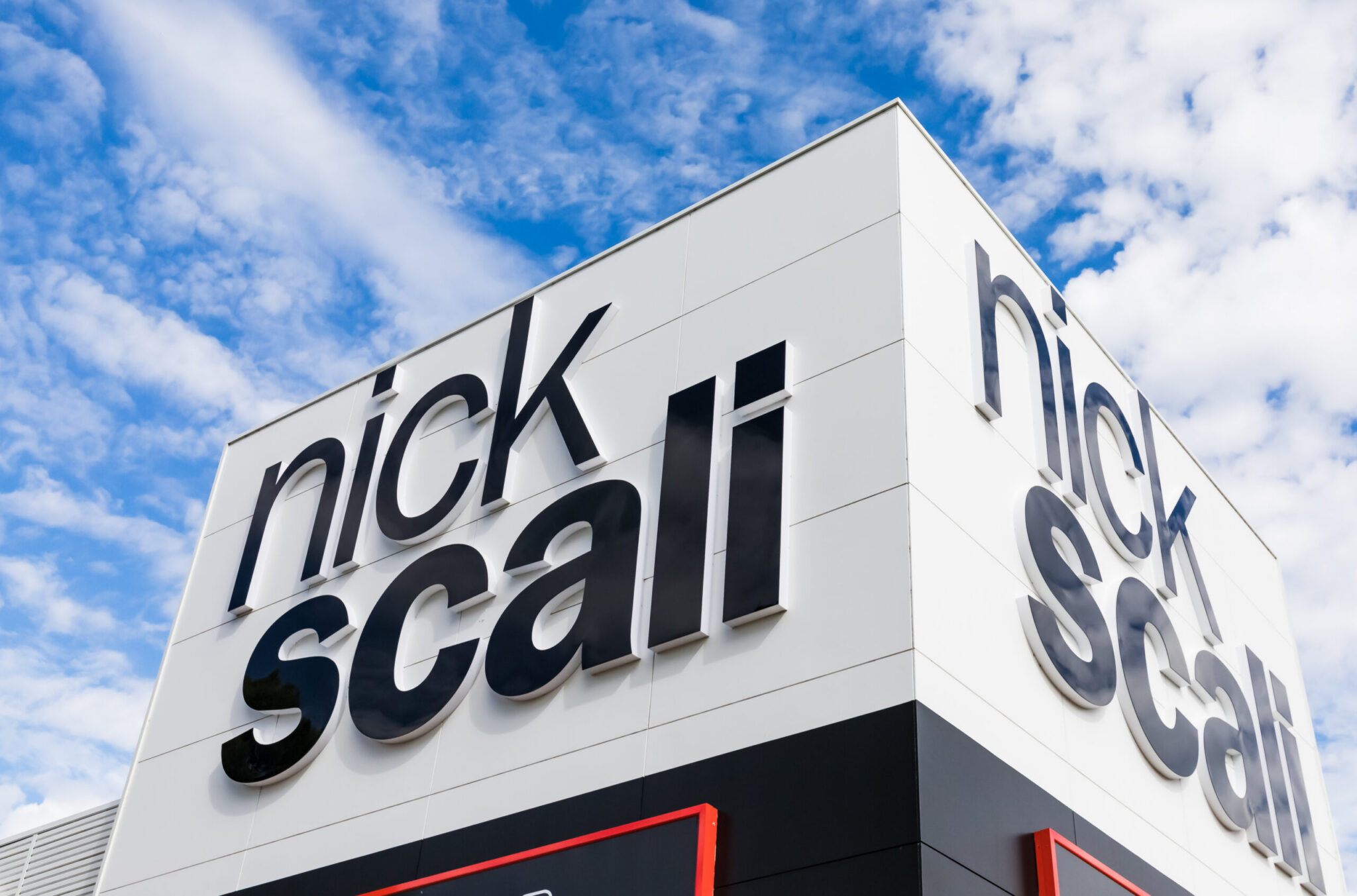 Exterior of a Nick Scali furniture store featuring large black Nick Scali signage on a white building against a blue sky.