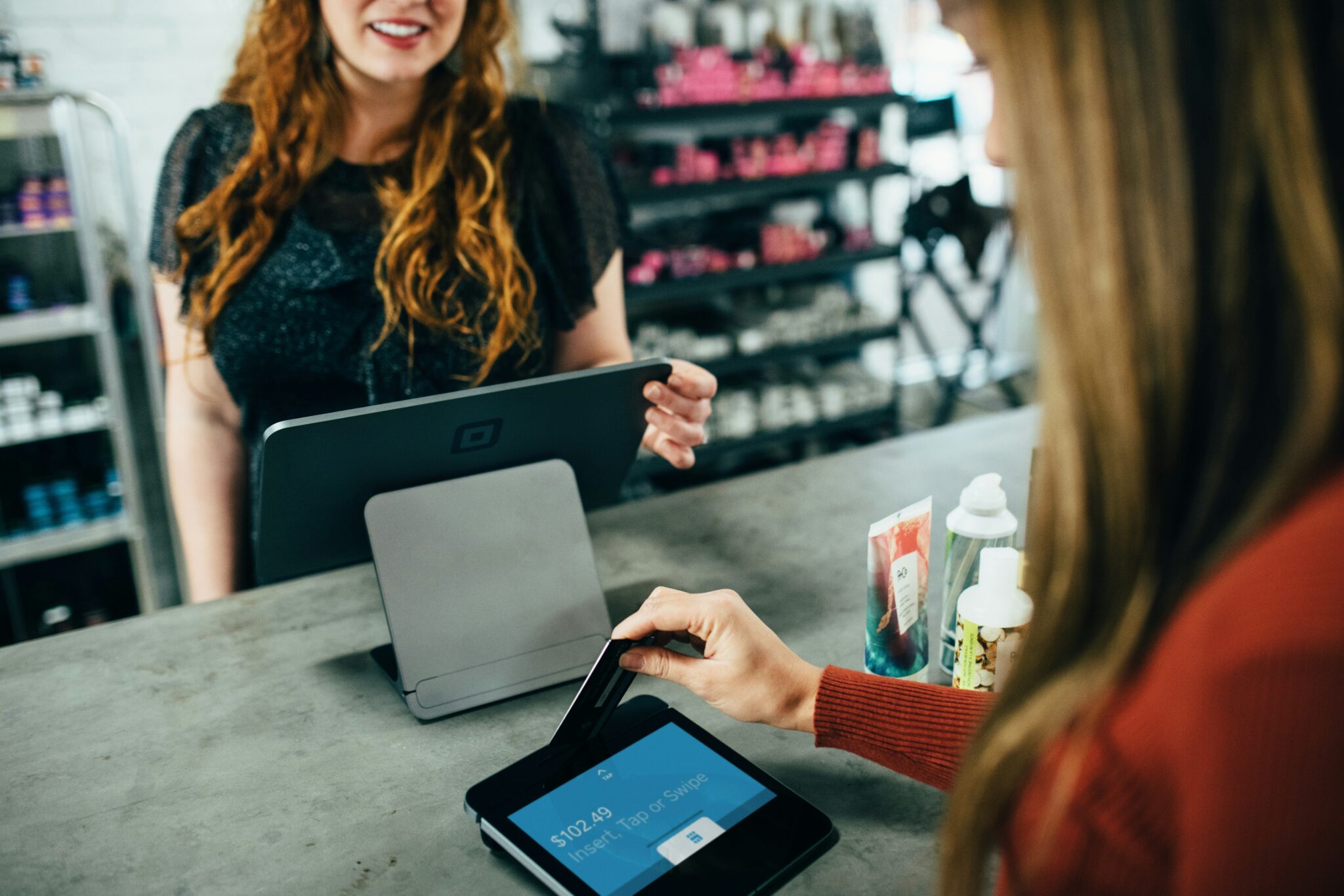 Customer paying by credit card at a retail checkout counter while a sales assistant operates a point-of-sale system.